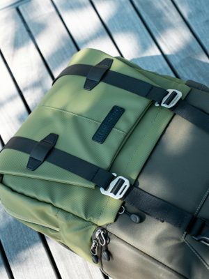Close-up of an olive green backpack on a wooden surface under soft sunlight.
