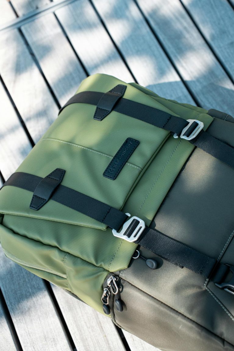 Close-up of an olive green backpack on a wooden surface under soft sunlight.