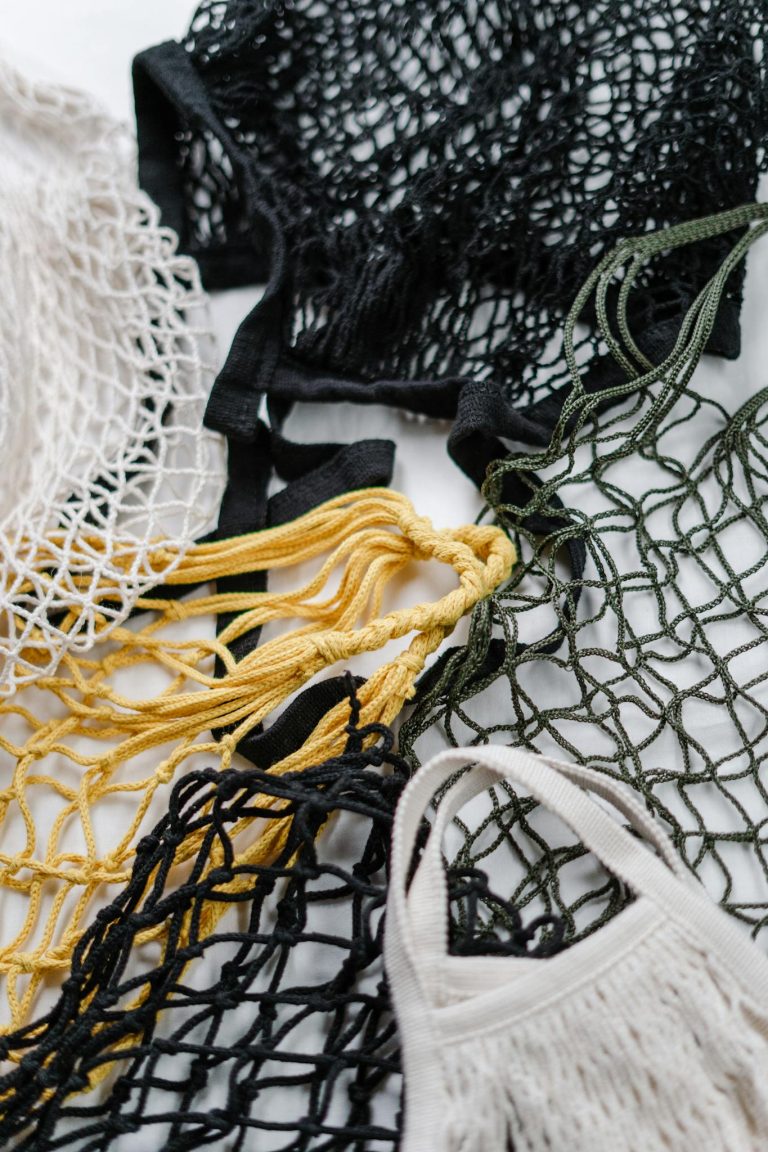 Close-up of various colored reusable mesh bags on white background.